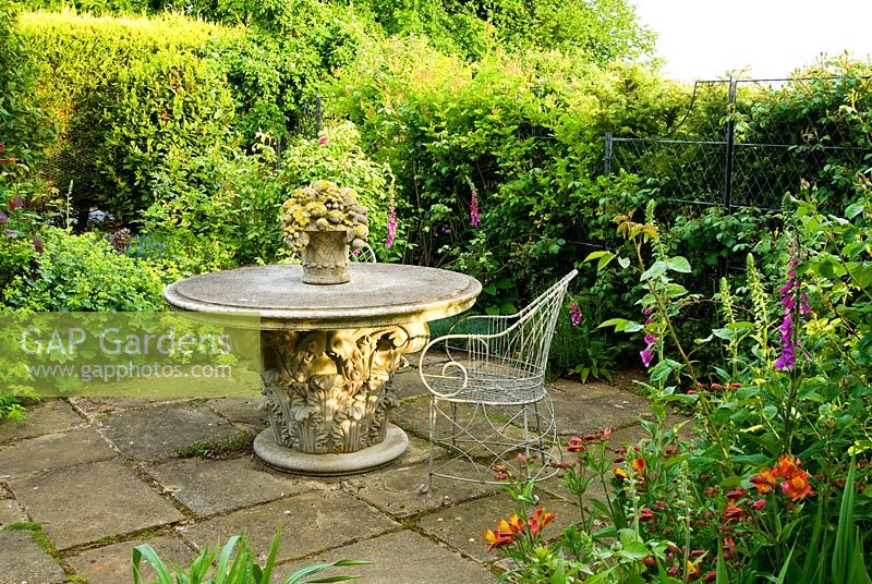 Stone table and wirework chair on small patio beside house with orange Alstroemerias. Old Rectory, Kingston, Isle of Wight, Hants, UK