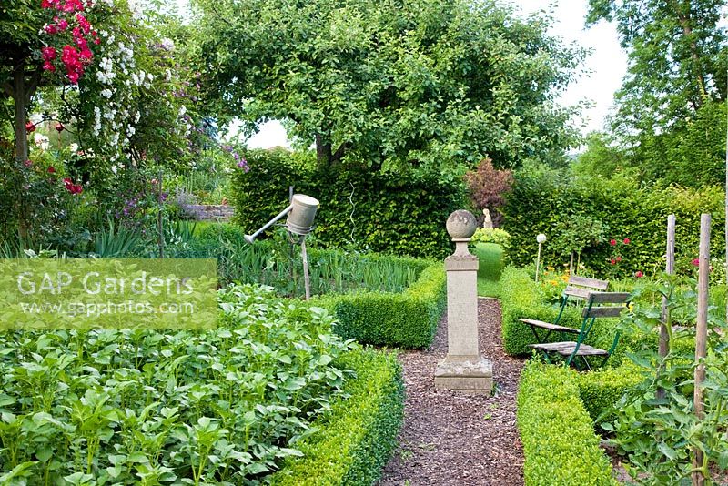 A stone plinth marks the centre of a Buxus - Box framed vegetable garden with Tomatoes, Potatoes and Beans