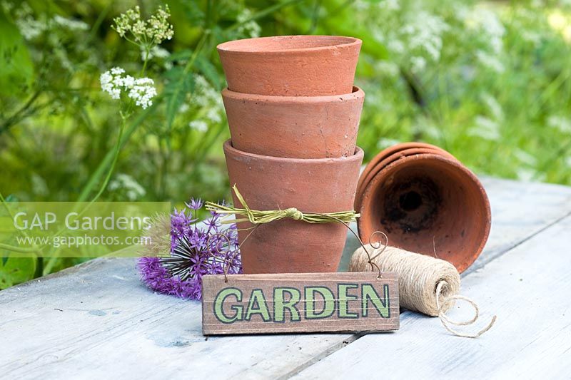 Decorative arrangement with alliums, stack of terracotta pots, string and garden sign