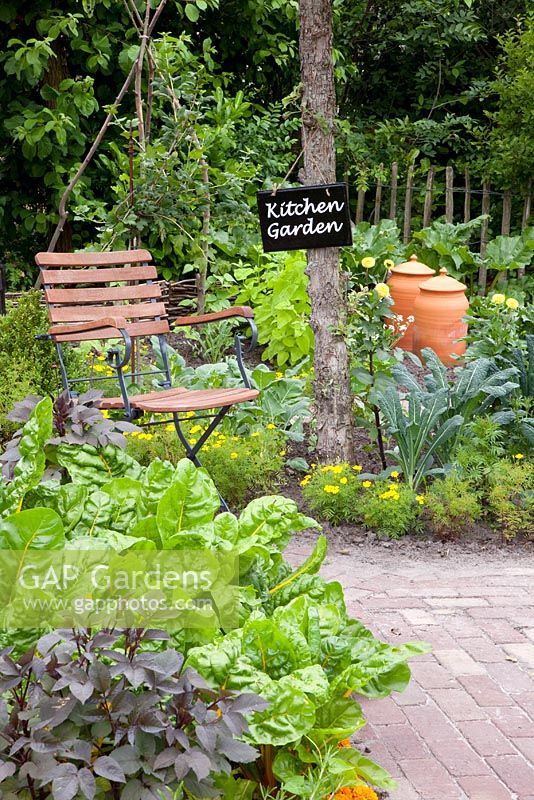 Potager with brick paths, wooden chair and beds with Brassica oleracea nero di toscana - Cavolo Nero, Beta vulgaris 'Bright Lights', Rhubarb forcer and Tagetes - Marigolds
