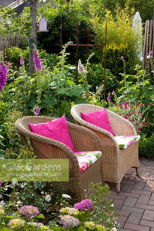 Small garden with wicker chairs surrounded by Digitalis - Foxgloves and Hydrangea - Scheper Town Garden

