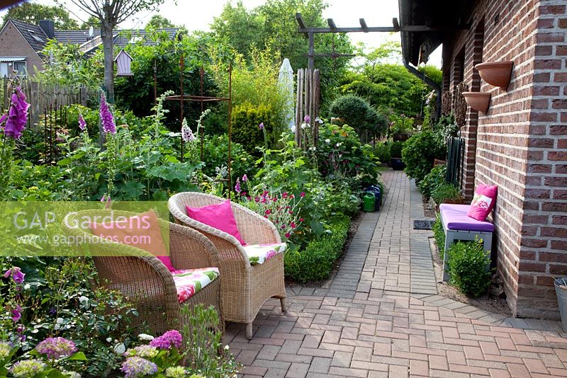 Small town garden with wicker chairs surrounded by Digitalis - Foxgloves and Hydrangea - Scheper Town Garden