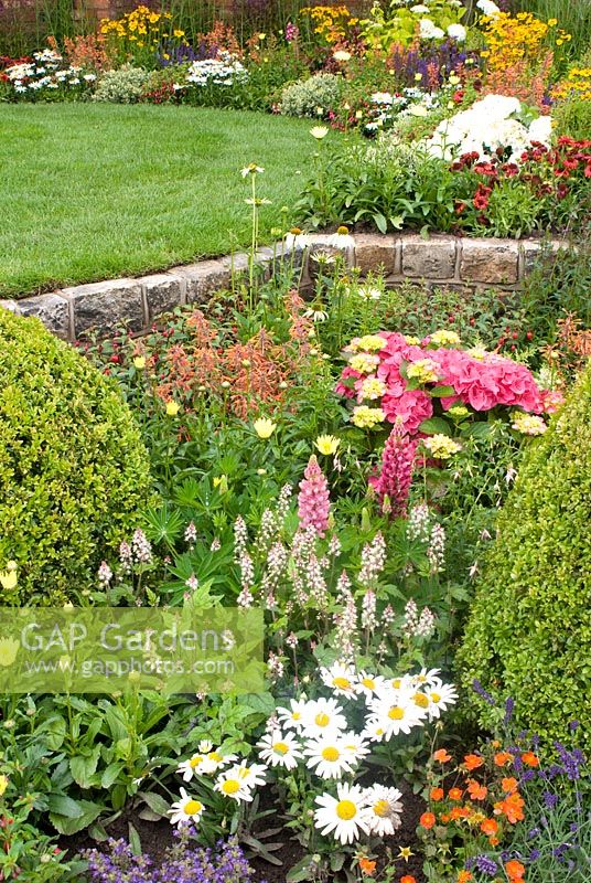 Raised lawn edged by colourful summer borders with perennials and Buxus. Russell Watkinson Landscapes 'Serenity' garden designed by Russell Watkinson. RHA Tatton Flower Show 2011