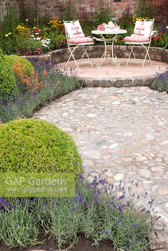 Cobbled path leading to seating area with colourful summer borders with Buxus topiary and Lavandula. Russell Watkinson Landscapes 'Serenity' garden designed by Russell Watkinson. RHA Tatton Flower Show 2011