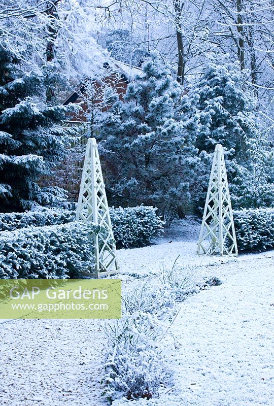 Formal town garden with wooden obelisks covered in snow, Oxford, UK. 
