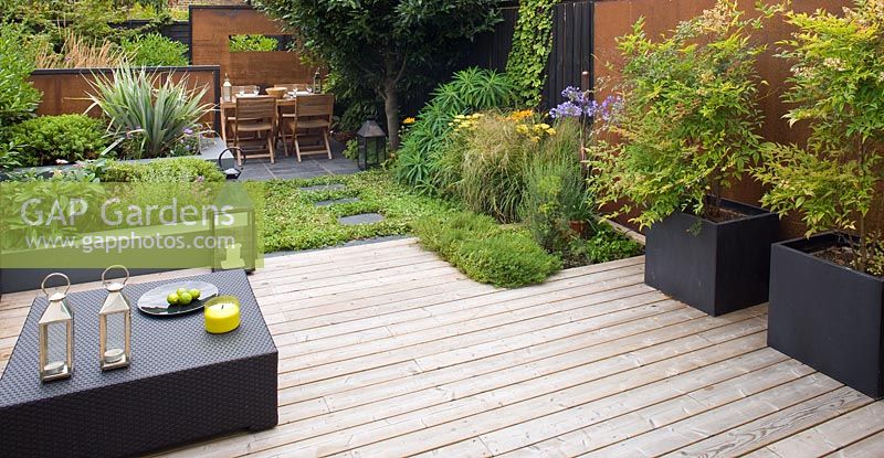 Small town garden with decked patio, screens made of mild steel, black planters and coffee table, London 
