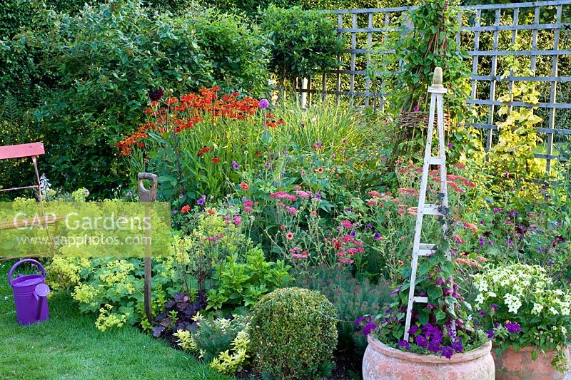 Colourful summer border with pots, seat and purple watering can