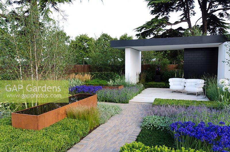 Cor-Ten steel water trough surrounded by Agapanthus, Stipa tenuissima and Lavandula, next to a black and white pavilion with white chairs - 'Vestra Wealth's Gray's Garden', Gold Medal Winner, RHS Hampton Court Flower Show 2011