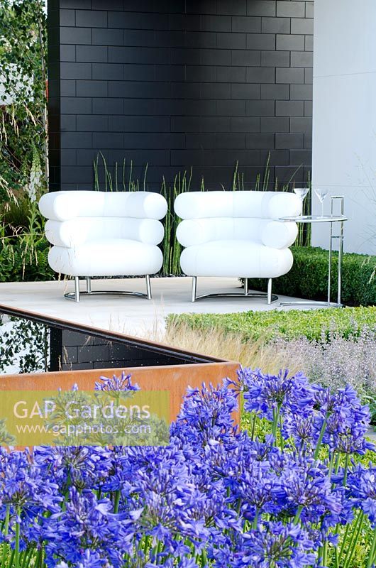 White chairs on a black and white pavilion next to a Cor-Ten steel water trough surrounded by Agapanthus and Stipa tenuissima and Box hedging . 'Vestra Wealth's Gray's Garden', Gold Medal Winner, RHS Hampton Court Flower Show 2011 