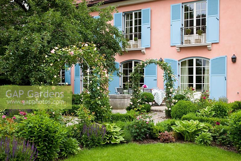 House with blue window shutters and garden with Rose arches of Rosa 'Pierre de Ronsard'  - Handbag Garde, Freising, Germany