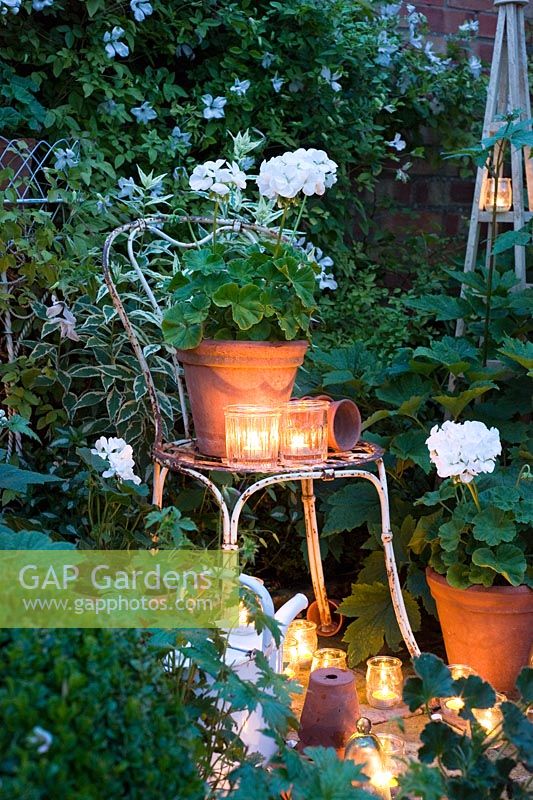 Glass jar tealights lighting white geraniums in containers in white garden