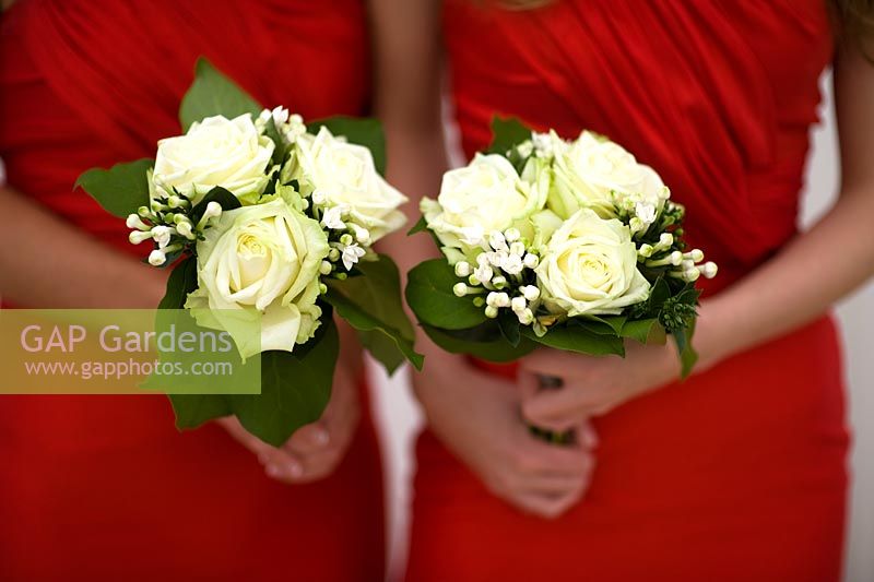 bridesmaids in red dresses holding bouquets of white roses