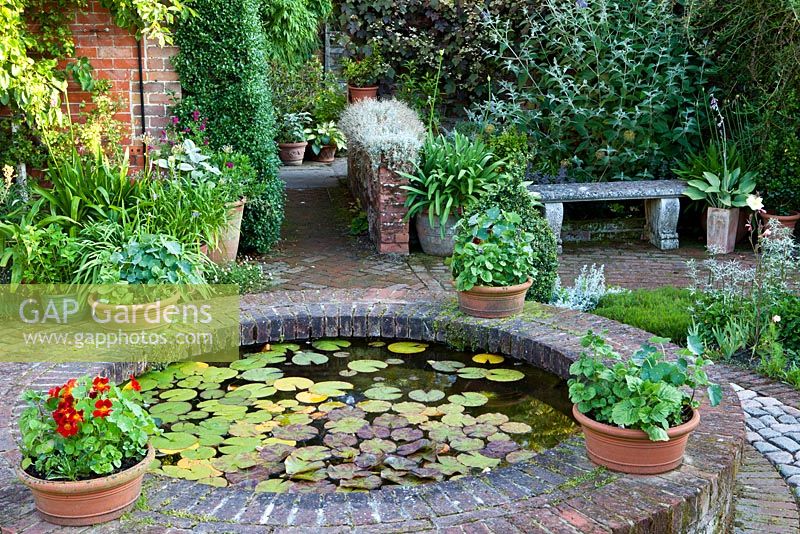 Summer garden, small brick circular pond with Nymphaea - The Corner House, Wiltshire. 