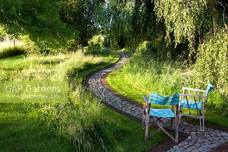 Summer garden, cobble and brick paths wend their way through informal borders - The Corner House, Wiltshire. 