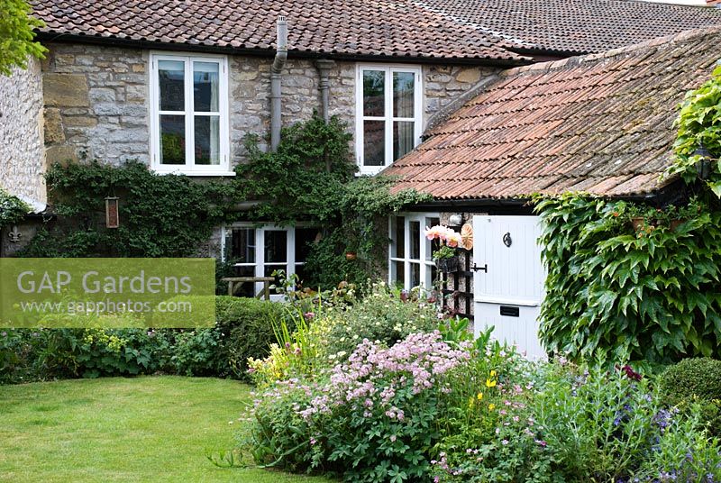 Cottage garden with border edging a lawn, plants include Astrantia major, Geranium sanguineum and Helianthemum  - Dunromin, Somerset
