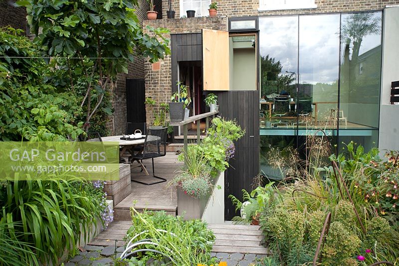 Seating area on decked patio surrounded with raised beds and containers, Deborah Nagan, garden, London
 