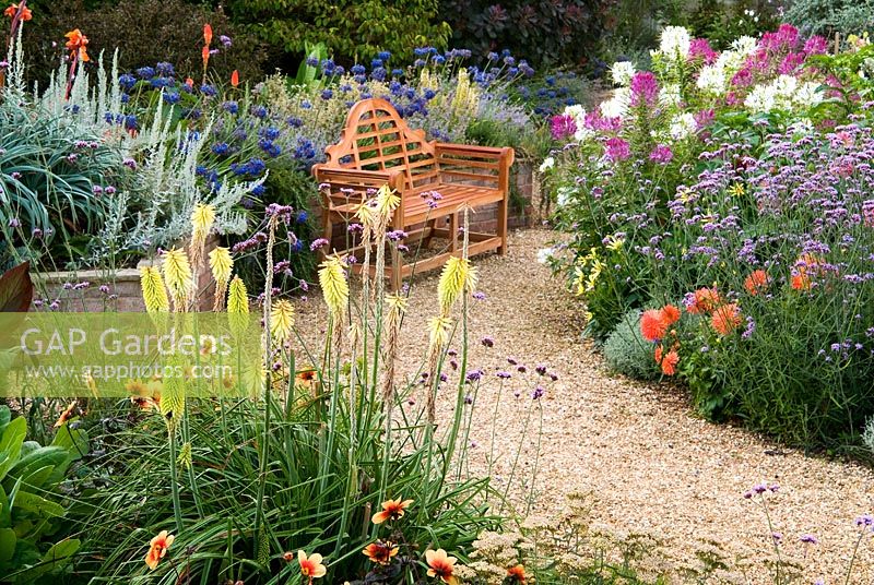Gravel paths through the sunken garden are edged with a mass of colourful perennials and annuals including Cleomes, Agapanthus, Eucomis, Dahlias, Verbena bonariensis and Kniphofias - Isle of Wight, UK
