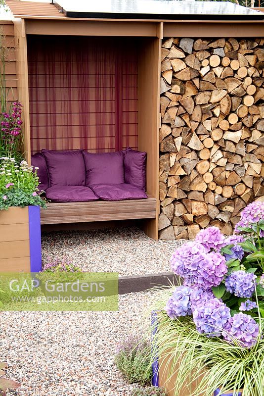 Wooden bench in shelter with log store and solar panel on roof. Hydrangea, Grasses, Thyme, gravel path - 'Futureproof - Waterproof' garden  - RHS Tatton Park Flower Show 2011