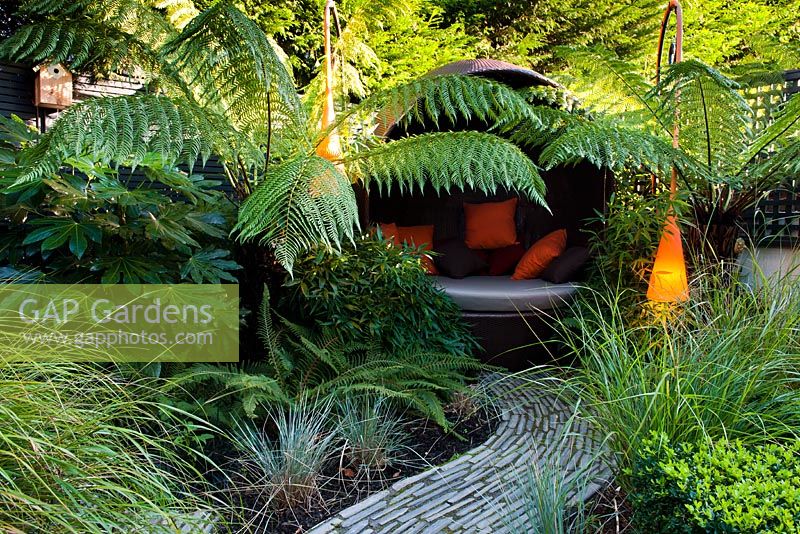 Contemporary light and covered seat surrounded by Dicksonia antarctica and Polystichum setiferum ferns 