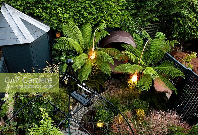 Contemporary suburban garden with seating areas and lighting surrounded by Dicksonia antarctica and Polystichum setiferum 