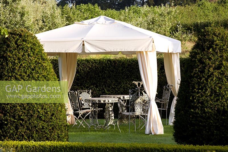 A canvas gazebo with metal table and chairs in formal country garden 