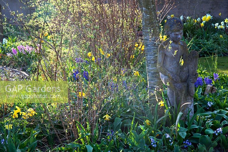 Sculpture in mixed Spring border with Hyacynths and Narcissus