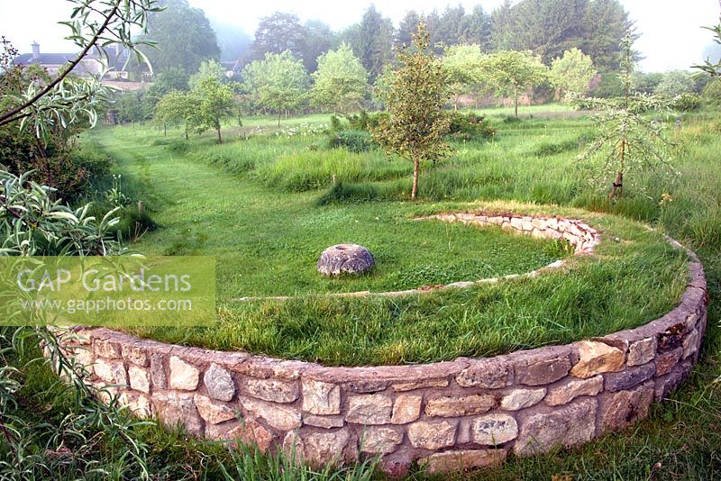 Grass covered stone horse-shoe shaped seat in meadow garden 