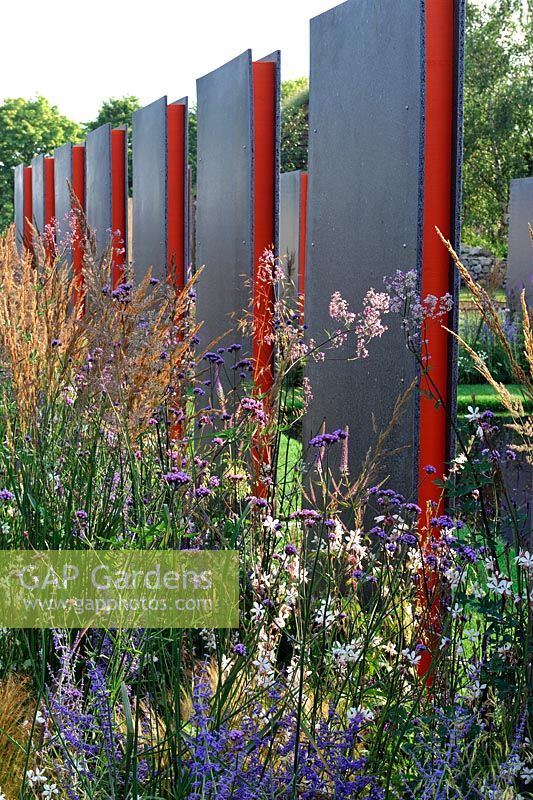 Late summer planting along a wall of repeating vertical panels of recycled plastic with granite-like effect