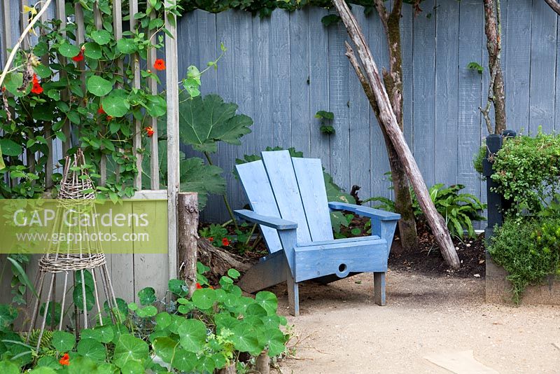 Tropaeolum - Nasturtiums on trellis. Blue chair and stained fence on patio - La Laboratoire - 20th International Garden Festival, Chaumont sur Loire, France 
 