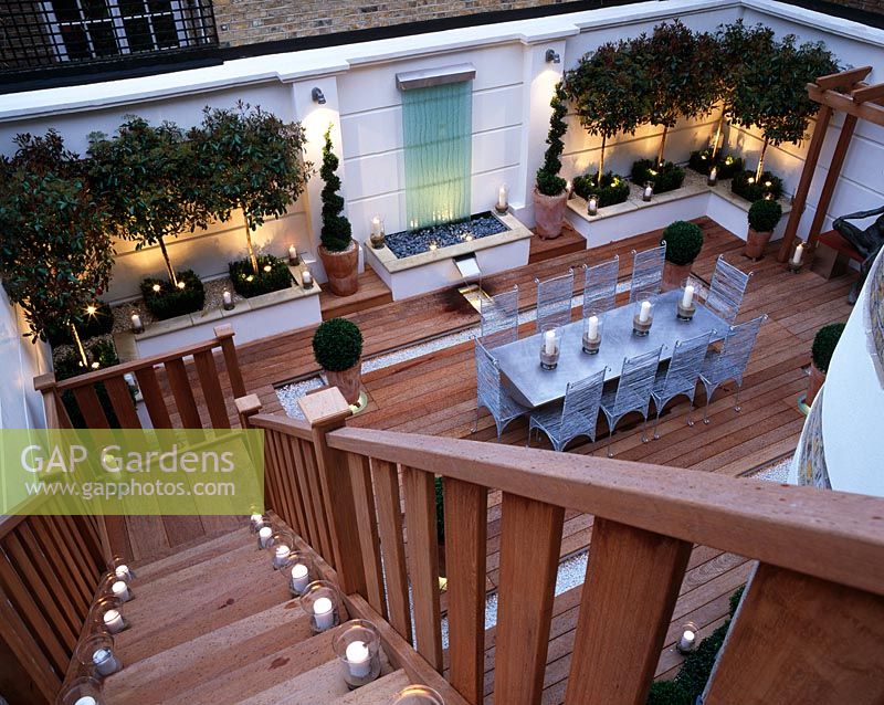 Roof garden with decking, glass water feature, clipped box, standard Photinias, silver table and chairs