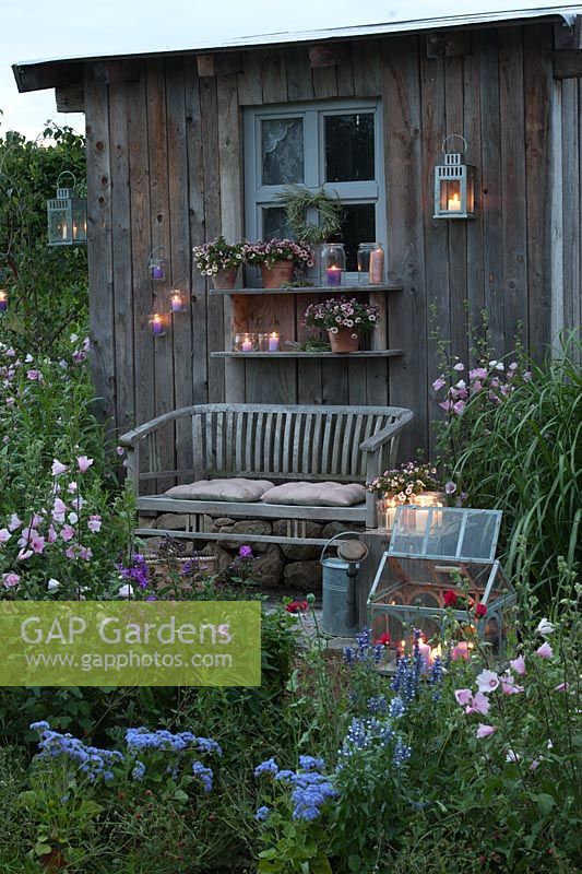Wooden summerhouse and patio lit up at night - Lavatera, Phlox, Miscanthus