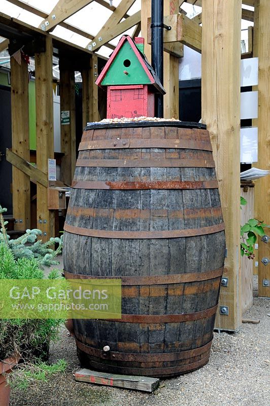 Large wooden rainwater barrel for recycling water from the roof with house shaped bird nest on top - Dalston Eastern Curve Garden, London Borough of Hackney, UK