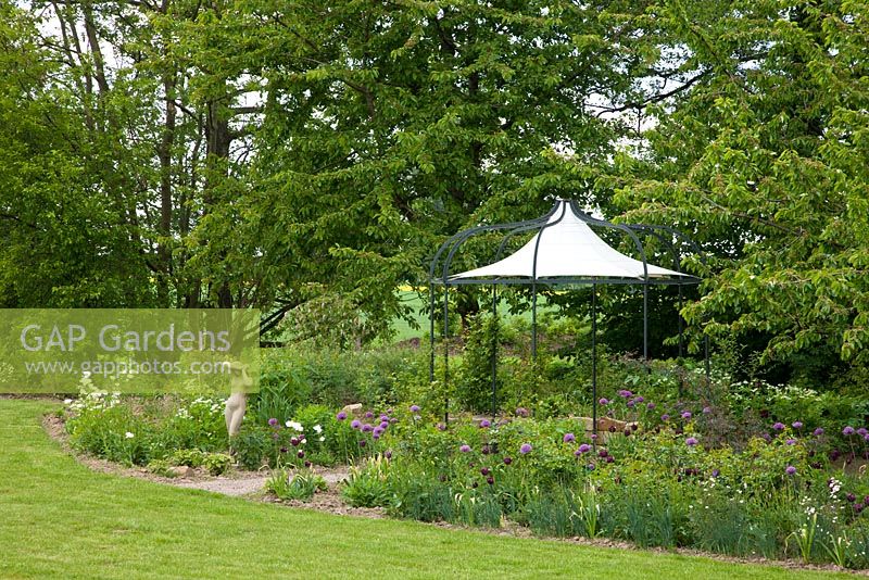 A pavilion and a female statue are features in a mixed border backed by trees - Prunus avium and Tulipa 'Queen of Night' - Jens Tippel
