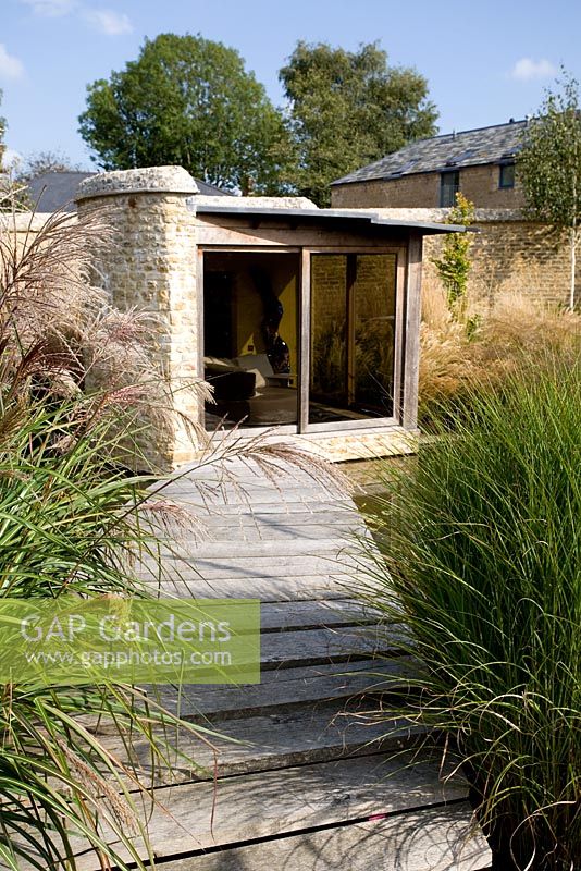 Garden view of the summerhouse with Miscanthus 'Malepartus' and 'Gracillimus' - Farrs, Dorset