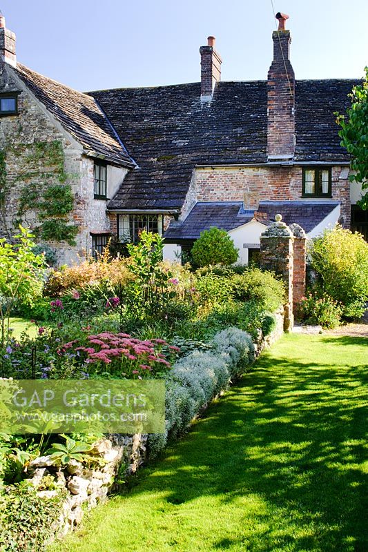 View to house with herbaceous border and low wall beside lawn - Barnwells, Cerne Abbas, Dorset.