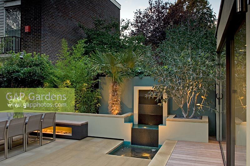 Urban courtyard garden lit up at dusk with decking, raised beds with Bamboo and water feature, London, UK
