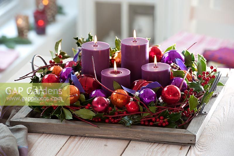 Christmas candles in wooden tray decorated with baubles, Cornus stems and Ilex - Holly berries

