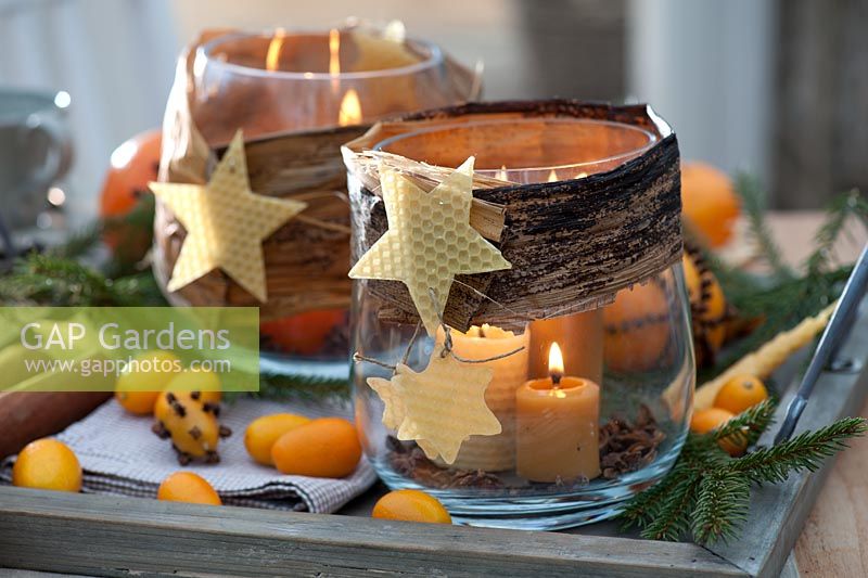 Beeswax candle lanterns decorated with wax stars, star anise, banana leaves, twigs of Picea, kumquat and orange