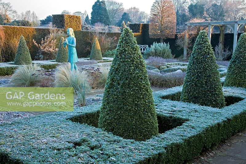 The formal knot garden with clipped box hedging and cone shaped pyramids. Statue of a girl holding the lamp of wisdom by Nathan David - Waterperry Gardens, Oxfordshire 