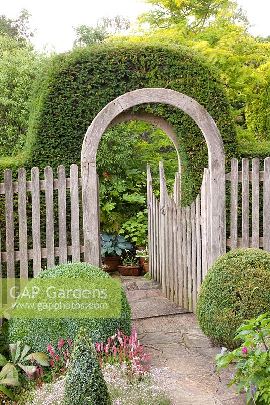 Curved gateway with clipped hedge growing over