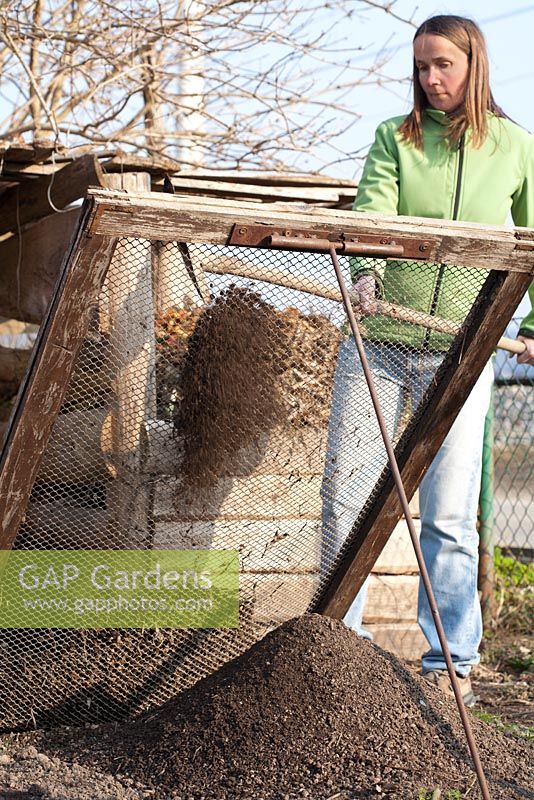 Woman sieving compost with shovel through the iron mesh to remove large lumps