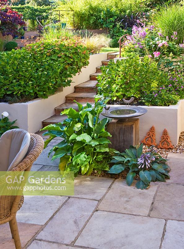 View from patio to path in terraced urban garden. Bronze bird bath on wooden pedestal