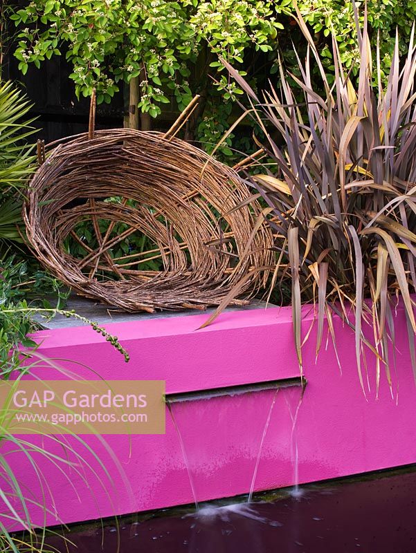 Woven willow sculpture above pink rendered wall and letterbox fountain with Phormium
