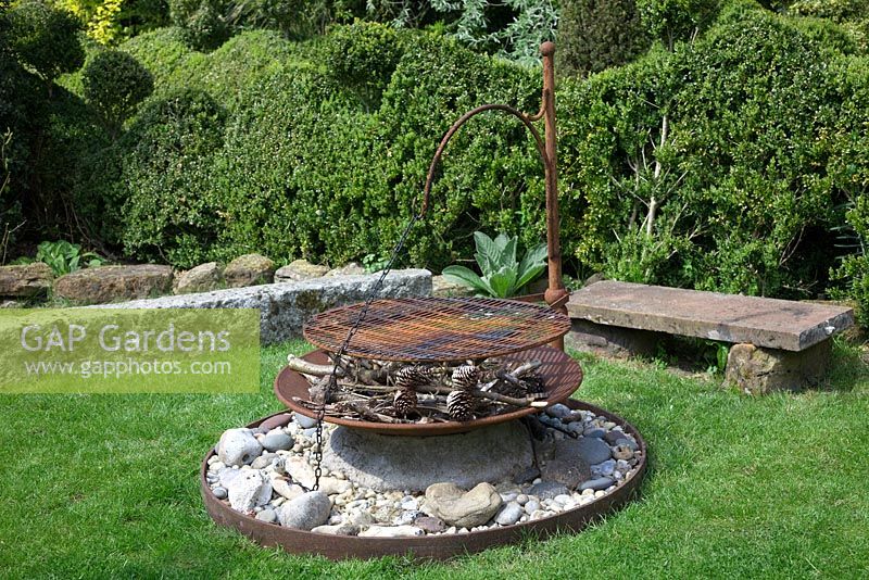 Rusty firepit sitting on a large stone boulder, with fir cones and kindling