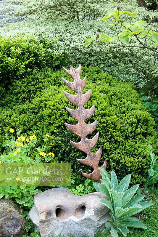 Metalwork sculpture with large flint stone and Buxus hedging. 
