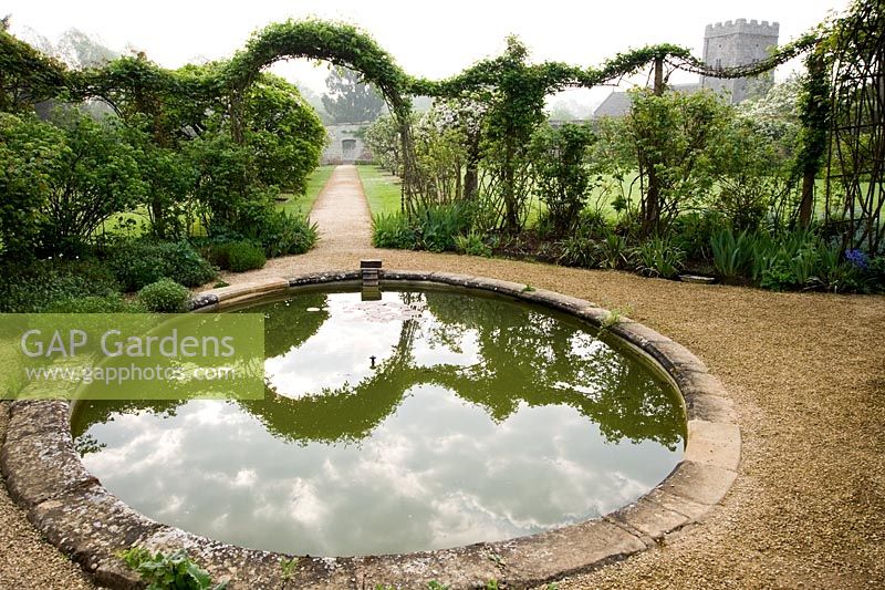 Circular pond in the Walled Garden surrounded by rambling roses trained over metal arches - Rousham House, Bicester, Oxon, UK