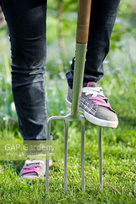 Teenager girl wearing sneakers with garden fork in the garden.