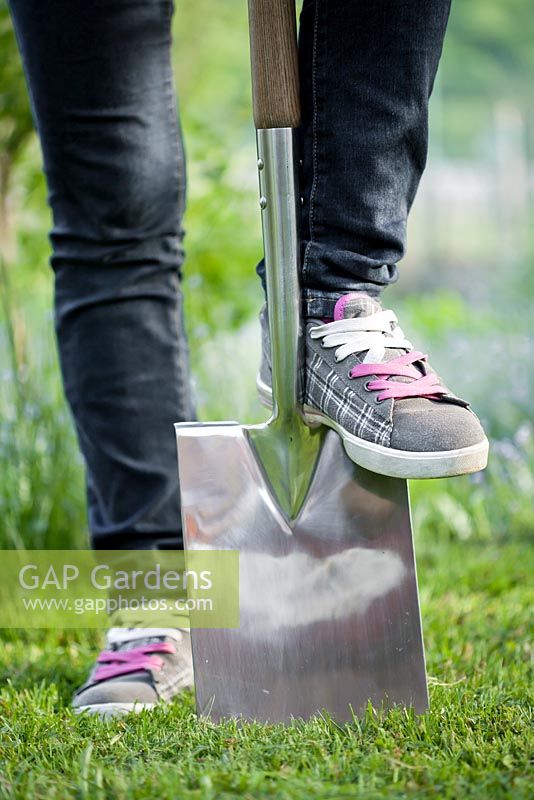 Teenage girl wearing sneakers with garden spade in the garden