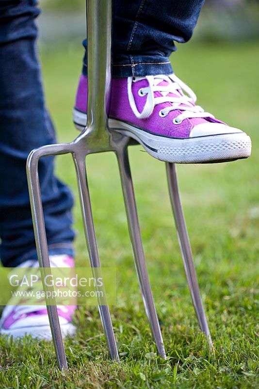 Teenage girl wearing sneakers with garden fork in the garden