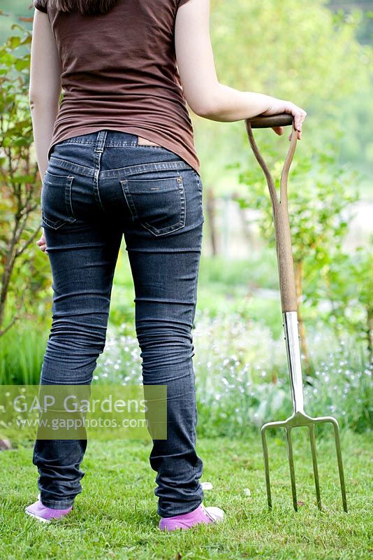 Teenager girl wearing sneakers with garden fork in the garden.